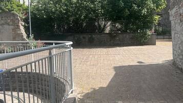 A paved courtyard with a metal railing, stone walls, and trees.