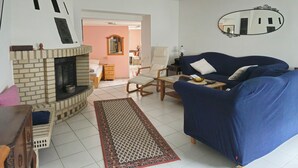 Ein Wohnzimmer mit Kamin, einem blauen Sofa, einem Holzstuhl und einem Essbereich im Hintergrund.