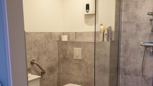 Ein modernes Badezimmer mit Duschkabine aus Glas, Toilette, Waschbecken und einem Händetrockner.