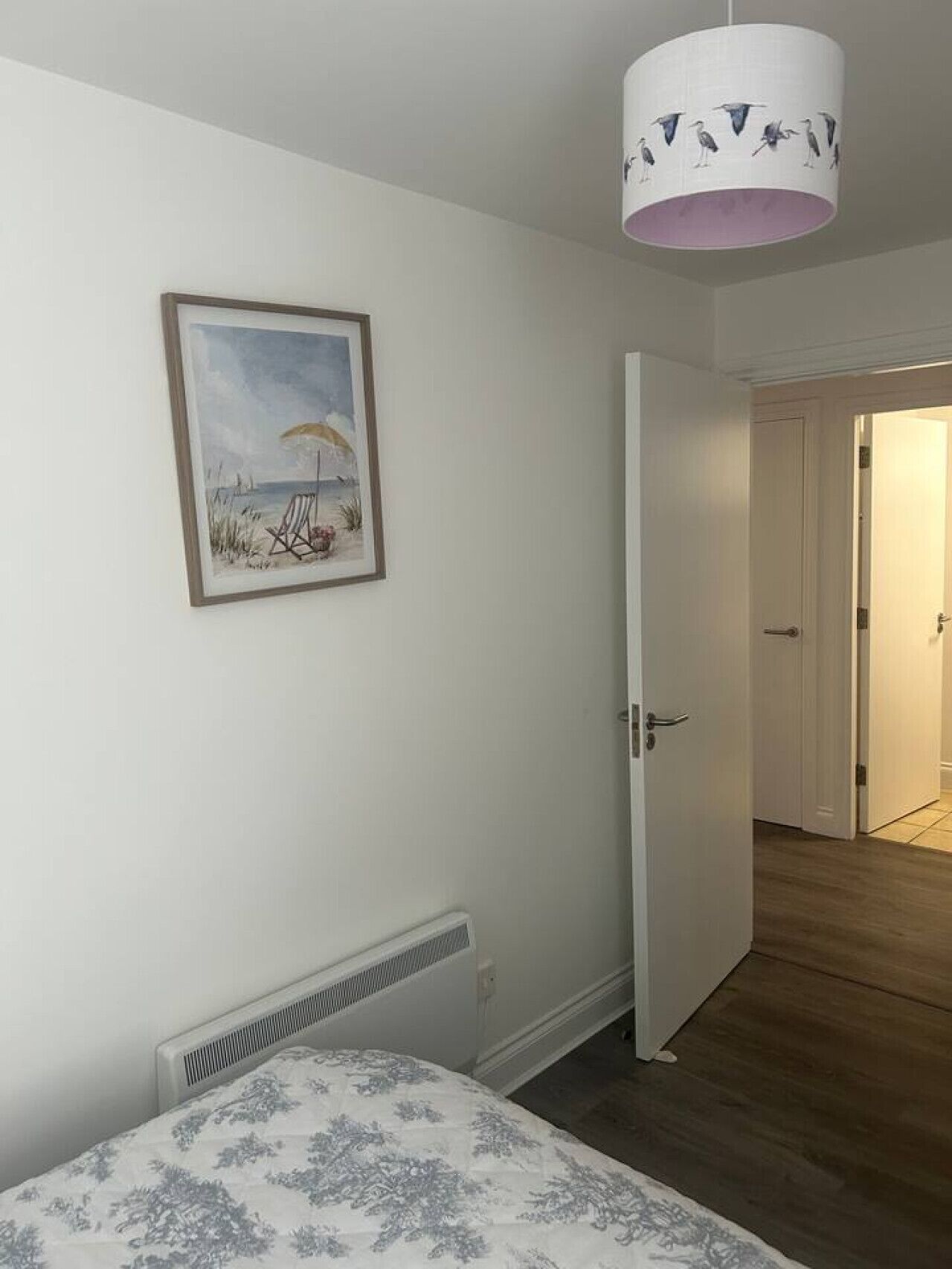 A bedroom with a bed, a radiator, a framed painting, and a door leading to another room.