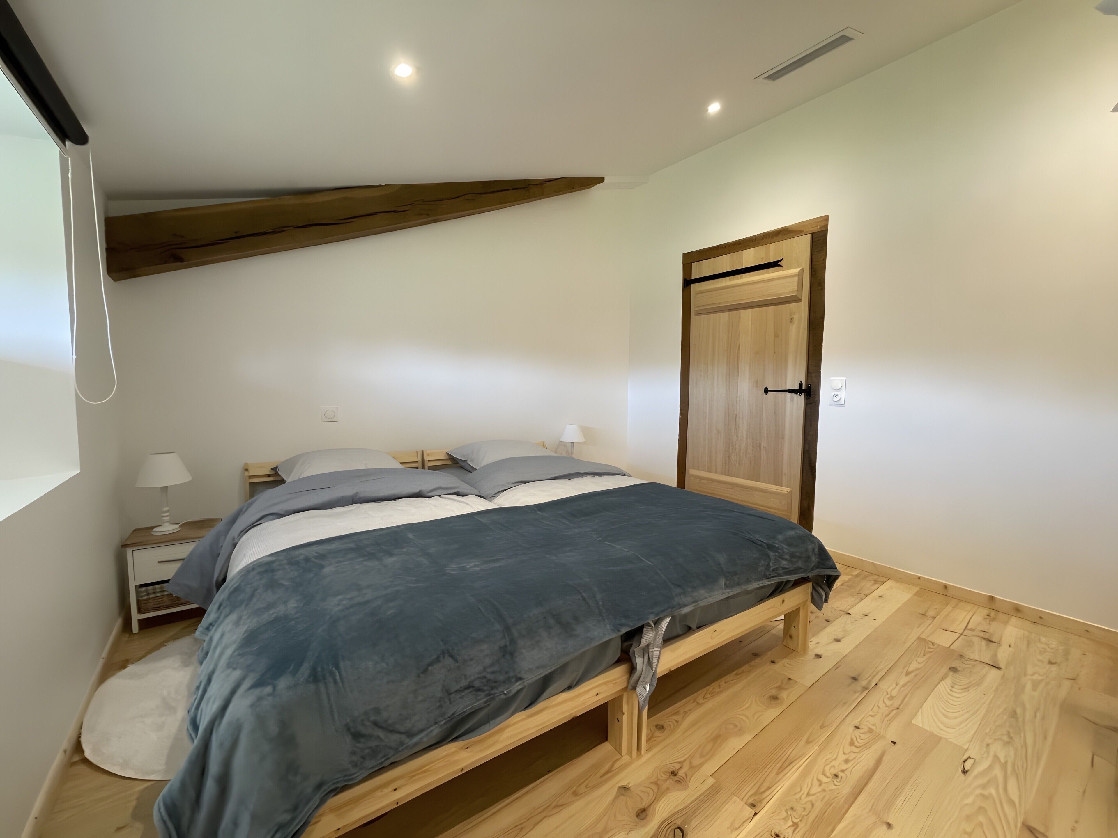 A bedroom with a bed, bedside tables, a wooden door, and a sloped ceiling.
