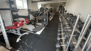 Uma academia com equipamentos de musculação, esteiras e um banco vermelho.