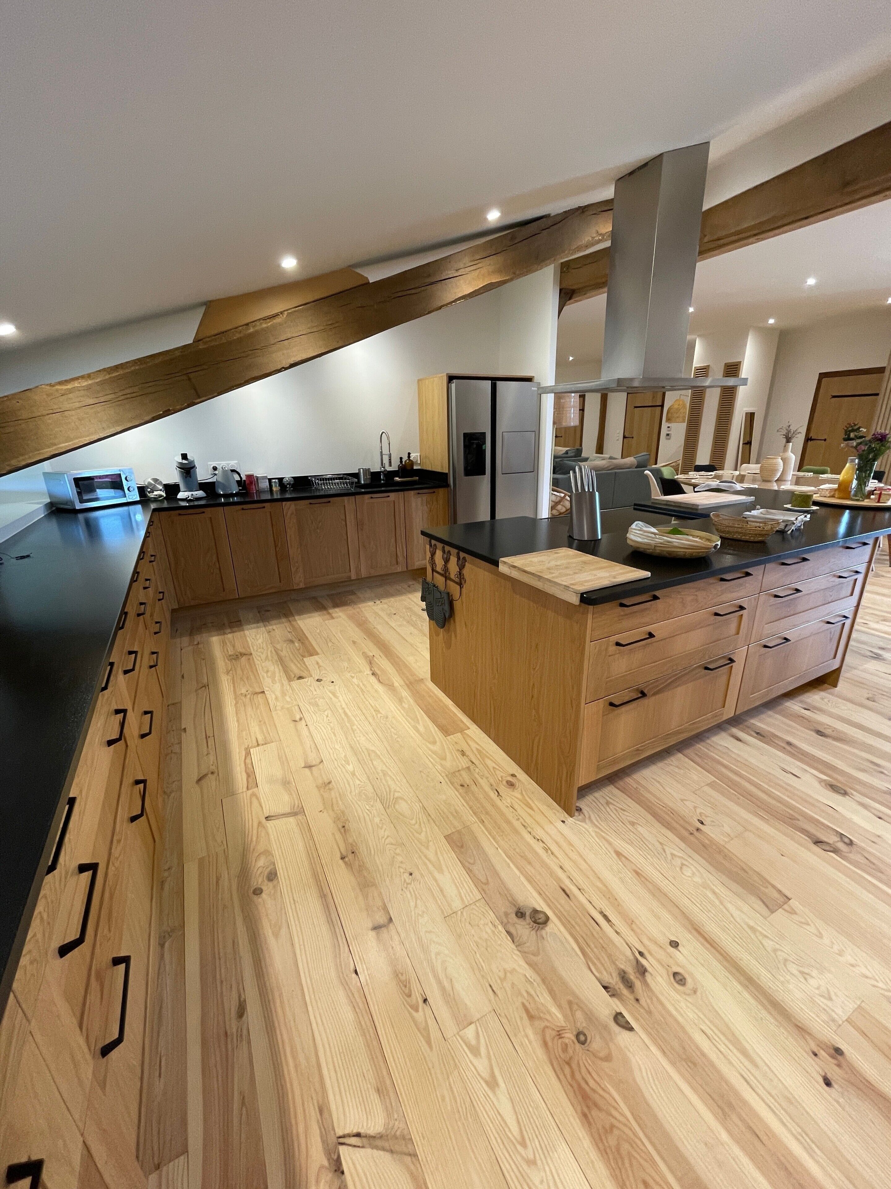 Une cuisine moderne avec des meubles en bois, un plan de travail noir et un réfrigérateur en acier inoxydable.