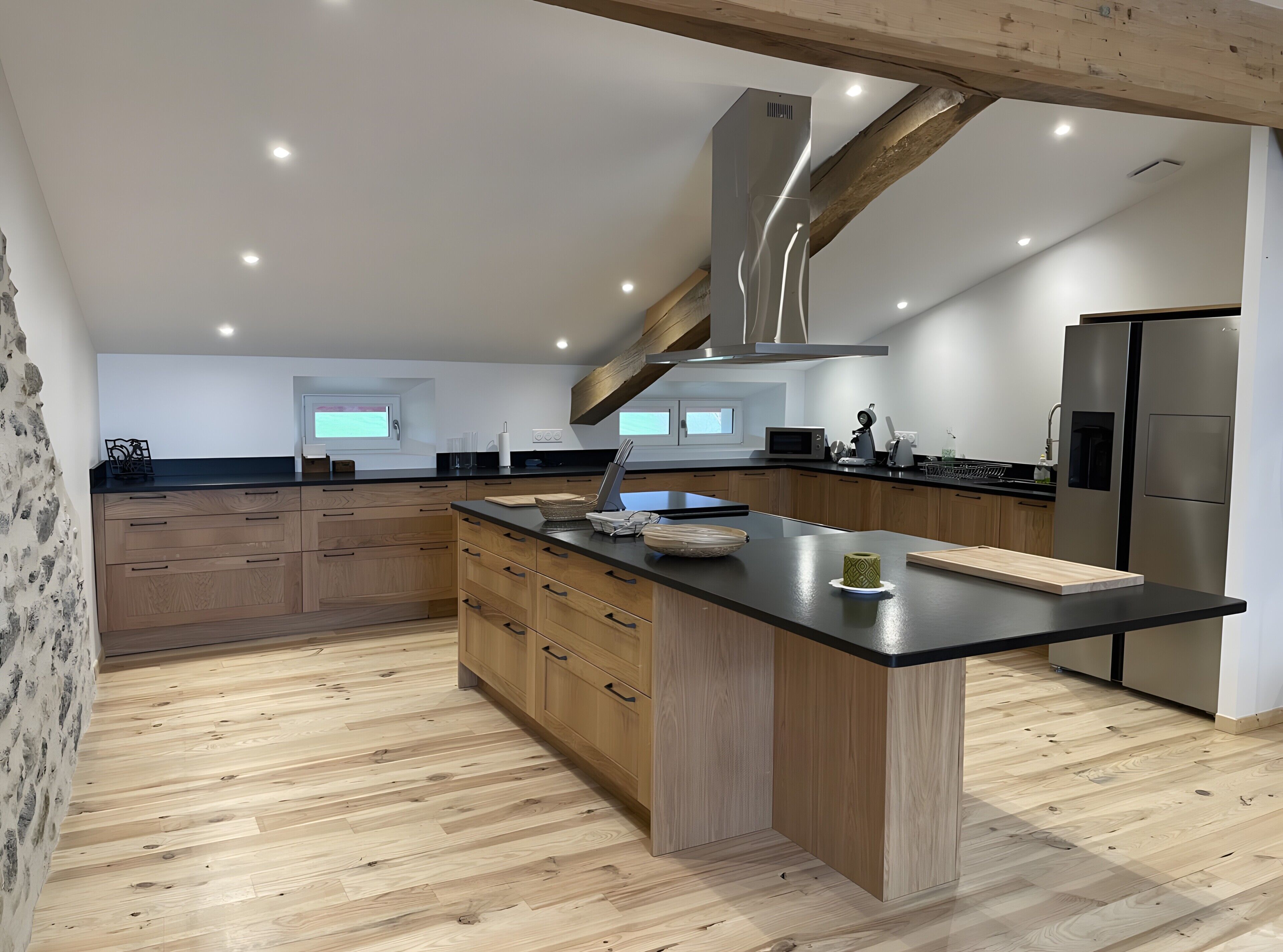 Une cuisine moderne avec des meubles en bois, un îlot central, des appareils en acier inoxydable et un éclairage encastré au plafond.