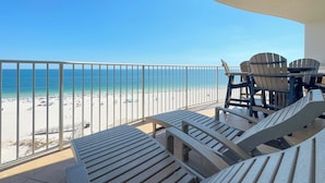 Un balcón con sillones de descanso y una mesa con vista a una playa y un cielo despejado.