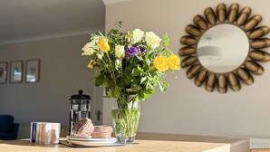 A dining table with a clear glass vase containing flowers, a coffee maker, and a plate with pastries. - 42 Little Trelyn (Wadebridge)