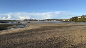 A coastal landscape with a wide sandy beach, a small body of water, and a distant town with buildings and hills. - 42 Little Trelyn (Wadebridge)
