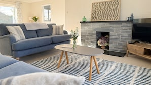 A modern living room with a grey sofa, a stone fireplace, a flat-screen TV, and a blue patterned rug. - 42 Little Trelyn (Wadebridge)