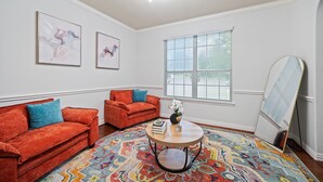 A room with two red sofas, a round coffee table, a colorful rug, and a large window with blinds. - Serenity of Spring, TX & The Woodlands - Modern 4BR Furnished Home (Spring)
