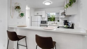 A modern kitchen with white cabinets, a microwave, a kettle, and two bar stools.