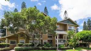A two-story residential building with a balcony on the second floor, surrounded by well-maintained lawns and trees.