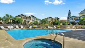 A swimming pool with lounge chairs and a hot tub, surrounded by apartment buildings.