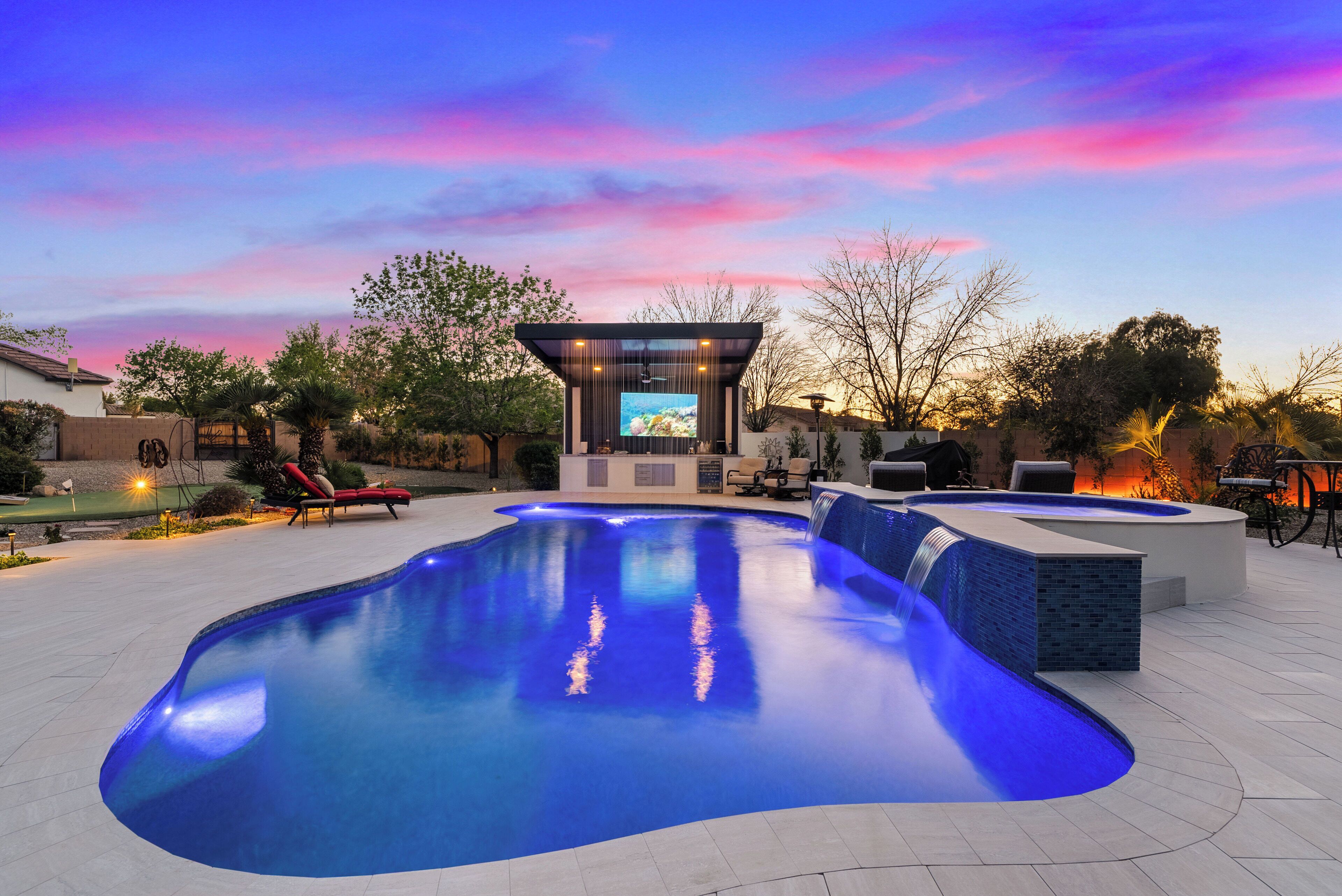Uma área de piscina moderna ao ar livre com hidromassagem integrada, espaço para sentar e um gazebo com tela de TV.
