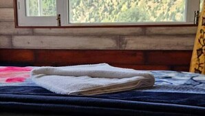 A room with a bed, a window with a view of a forested mountain, and a wooden wall. - Hotel Kelson Dx  (New Delhi)