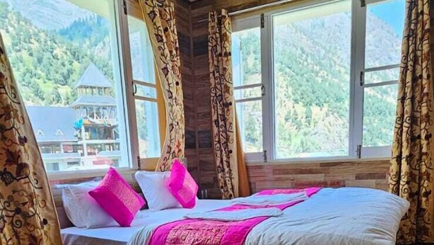 A wooden-floored bedroom with a bed, a glass table, and large windows offering a mountain view. - Hotel Kelson Dx  (New Delhi)