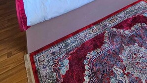 A bedroom with a wooden wall panel design, a bed with white bedding, and a red patterned rug. - Hotel Kelson Dx  (New Delhi)