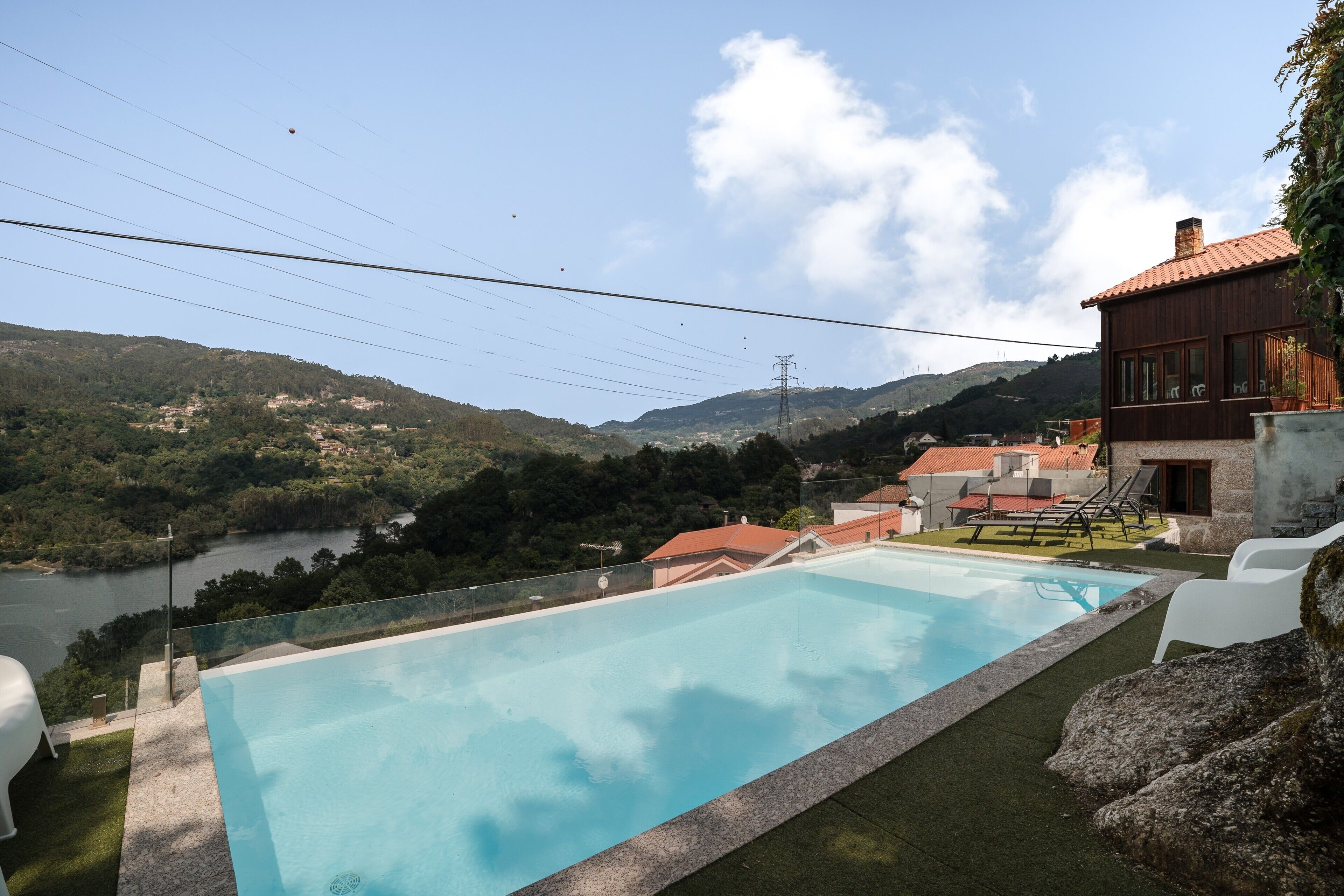 A swimming pool with a view of a lake and mountains, surrounded by a wooden building with a red roof.