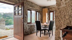 A room with stone walls, a wooden door, a dining table with chairs, and a view of a lake.
