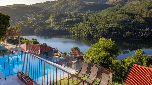 A pool with a glass barrier, a chair, and a view of a lake surrounded by hills.
