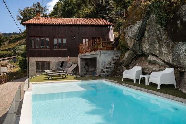 Une piscine avec des chaises longues, un mur en pierre et un bâtiment en bois avec un toit rouge.