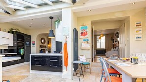 A modern kitchen with black cabinets, a central island, and a dining area with a table and chairs. - Harbour View House | Old Town, Sea Views | Sleeps 8 (North Yorkshire)