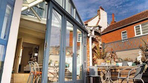 A modern house with a glass door leading to a patio area with outdoor furniture. - Harbour View House | Old Town, Sea Views | Sleeps 8 (North Yorkshire)