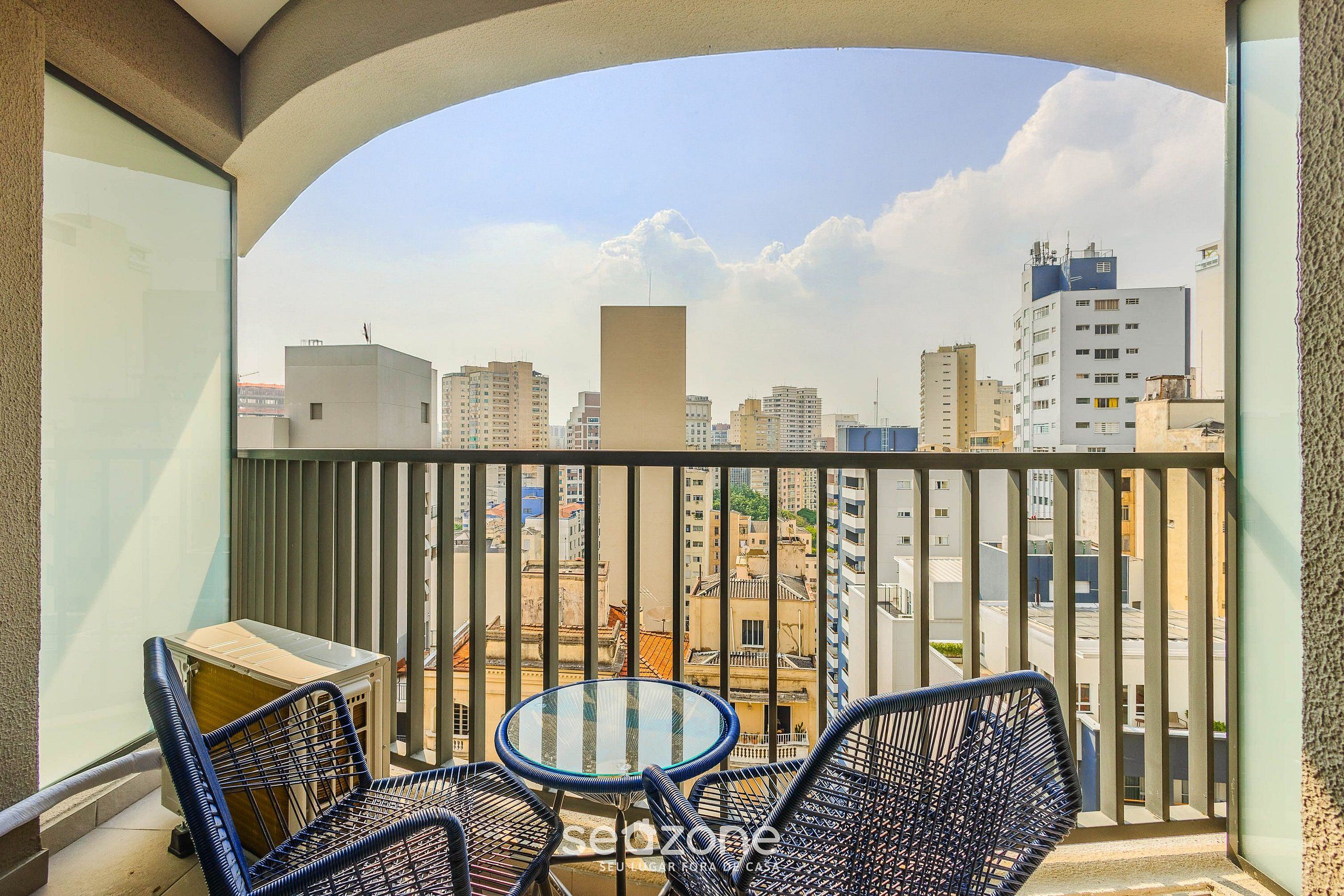 Varanda com mesa e cadeiras, oferecendo vista de um horizonte urbano com diversos edifícios.