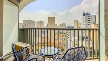 Varanda com mesa e cadeiras, oferecendo vista de um horizonte urbano com diversos edifícios.