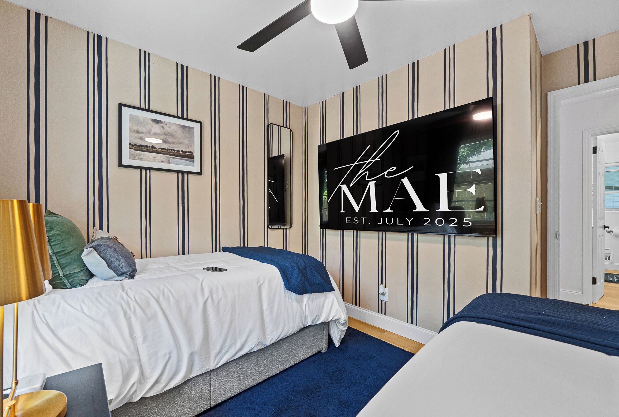 Une chambre d’hôtel équipée d’un lit, d’un bureau, d’une chaise, d’un ventilateur de plafond et d’un téléviseur fixé au mur.