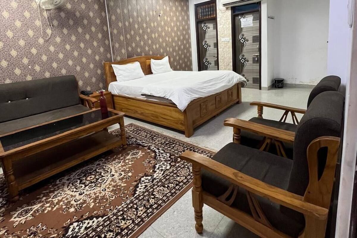 A bedroom with a bed, a sofa, a wooden chair, and a patterned rug.