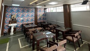 A dining area with multiple tables and chairs, a ceiling fan, and a decorative wall with floral patterns. - Staylo Masterprice Inn (Lucknow)