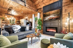 A cozy living room with a fireplace, wooden walls, and a comfortable seating area. - Romantic Cozy Smoky Mntn Cabin-Hot Tub-Loft Balcony-EV Chgr (Sevierville)