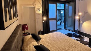 Een slaapkamer met een groot bed, een hoofdeinde, een nachtkastje, een lamp en uitzicht naar buiten door een glazen deur.
