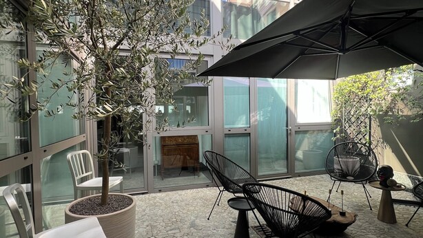 Een modern buitenzitgedeelte met stenen vloeren, metalen stoelen en een grote parasol.