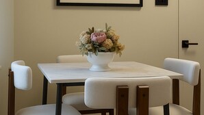 A dining area with a table and four chairs, a framed painting above the table, and a door to the right. - 3 KING Beds & Free parking • Central Place (Pittsburgh)