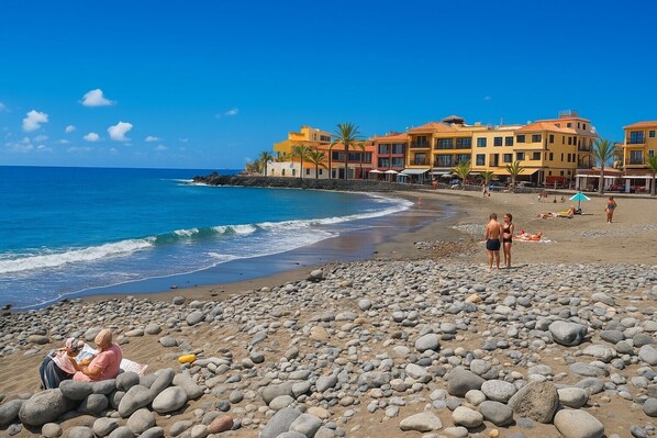 A beach with a rocky shore, a clear blue sky, and buildings in the background.