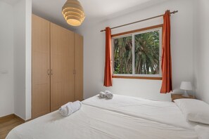 A bedroom with a bed, a wardrobe, a window with curtains, and a lamp.