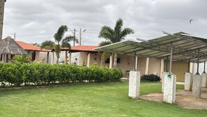 A covered outdoor area with a grassy lawn, a building with a red-tiled roof, and a pergola structure.