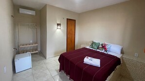 A bedroom with a bed, a wardrobe, a small refrigerator, and a wall-mounted light fixture.