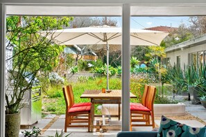 Un patio al aire libre con mesa y sillas, rodeado de abundante vegetación y una piscina.