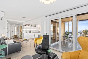 A modern living room with a sofa, a chair, a coffee table, and a dining area with a table and chairs.