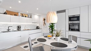 A modern kitchen with white cabinets, a central island, and a dining area with grey chairs.
