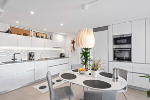 A modern kitchen with white cabinets, a central island, and a dining area with grey chairs.