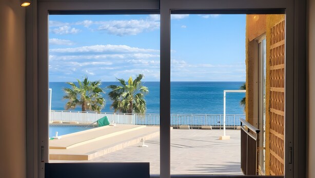 A view from inside a building to a pool area with a clear sky and palm trees.