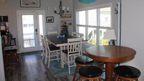 A dining area with a wooden table and chairs, a chandelier, and a view of the outdoors through large windows. - ISLAND PARK - SECOND ROW! AVAILABLE NOW! By Williamson Realty (Ocean Isle Beach)
