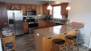 A modern kitchen with wooden cabinets, stainless steel appliances, a granite countertop, and two bar stools. - ISLAND PARK - SECOND ROW! AVAILABLE NOW! By Williamson Realty (Ocean Isle Beach)