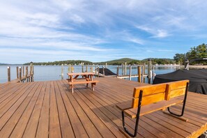 Une terrasse en bois avec une table de pique-nique et un banc, offrant une vue sur un lac paisible, avec des quais s’avançant dans l’eau.