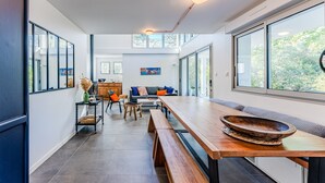 A modern interior with a long wooden table, benches, and a large window offering a view of greenery.