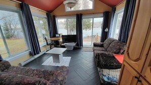 A cozy living room with a sofa, a coffee table, and a TV. There are large windows and a view of the outdoors.