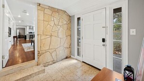A hallway with a stone accent wall, a wooden floor, and a view of a kitchen and dining area. - Wonder World Retreat (San Marcos)